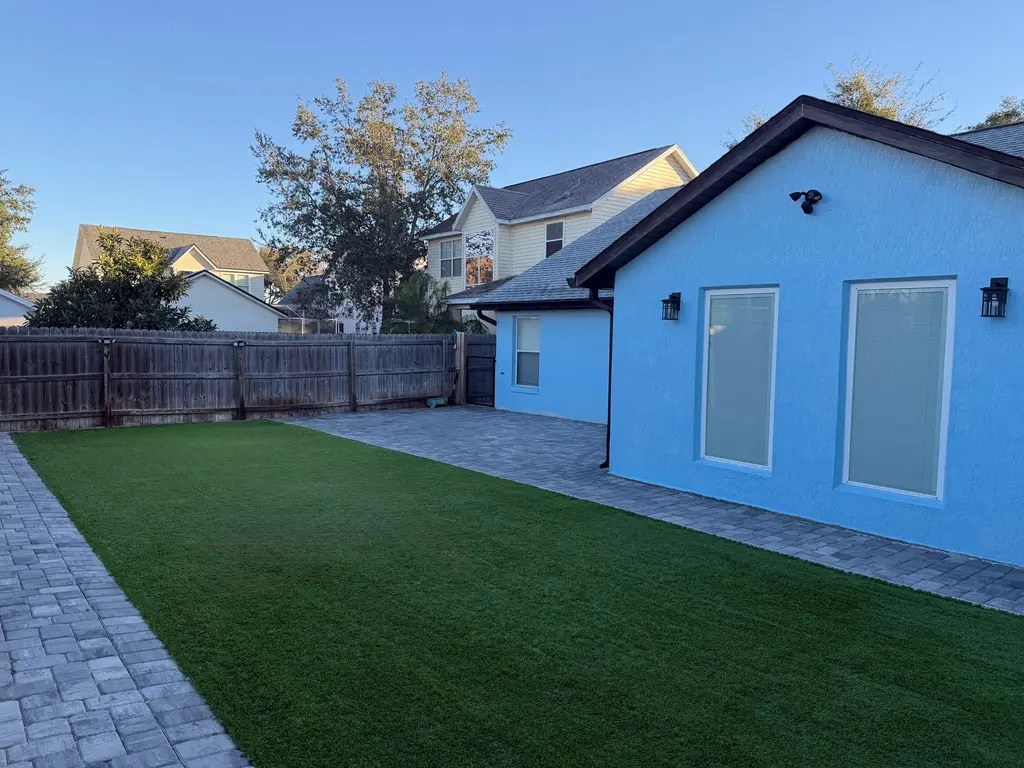 A fenced backyard with artificial grass and a paver patio